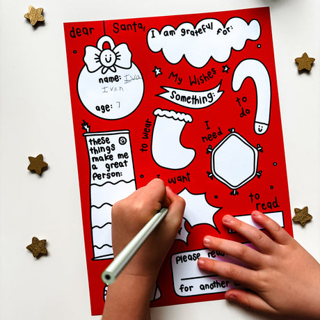A child is writing a personal letter to Santa Claus on a red A4 card with a Christmas theme. The card has illustrations of Santa, a reindeer, and stars, and includes prompts for the child to write about their proud moments and what they want to gift to someone.