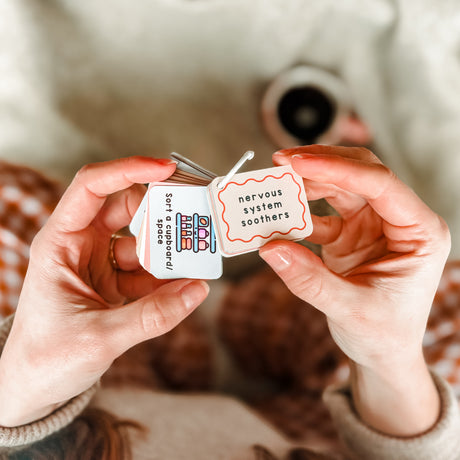 Hands holding two small containers labeled 'nervous system soothers' with a blurred background.