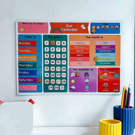 Children's educational calendar on a white wall with colorful stationery items below.