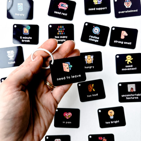 Hand holding a black tag with a symbol and text, surrounded by various other tags on a white background.